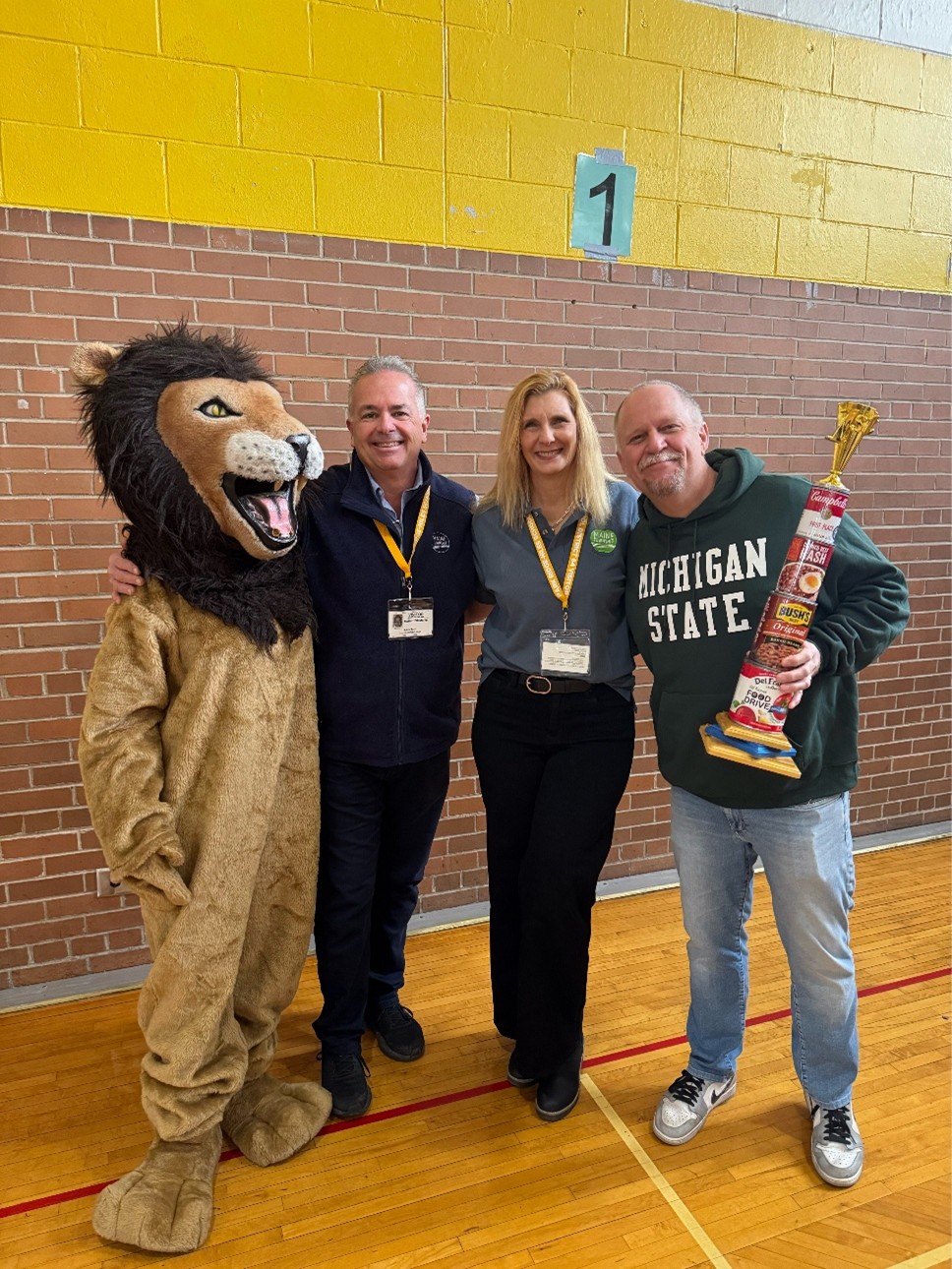 3 people and a lion mascot holding awards